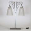J. Vandôme & Muller Frères Lunéville, vers 1930 Lampe Art Déco à deux lumières en métal martelé nickelé et verrerie signée.  Structure en potence à deux bras terminés par d’élégantes volutes martelées, surmontant un fût vertical en métal à décor rayonnant. La base rectangulaire est signée J. Vandôme, artisan ou maison d’édition réputée pour ses œuvres de ferronnerie décorative dans les années 1930