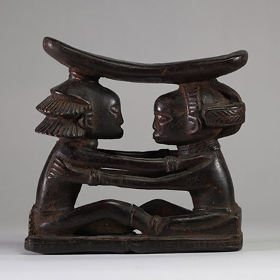 Ancien appui-nuque Luba « Shankadi », Congo RDC. Très bel exemplaire représentant deux figures humaines assises face à face, les bras posés sur les épaules de l’autre, dans une posture d’étreinte rituelle. Chacune soutient une tablette repose-nuque incurvée. L’une des figures présente une coiffure en croix (tulume) et l’autre une coiffure en cascade ( dans la tradition du maître de Kalundwe) . Les