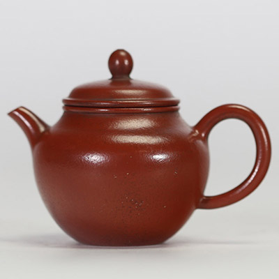 Théière globulaire en terre cuite pourpre, dite zisha, typique de la production de Yixing. Elle présente un panse arrondi, un court bec conique et une anse semi-circulaire.
