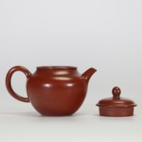 Théière globulaire en terre cuite pourpre, dite zisha, typique de la production de Yixing. Elle présente un panse arrondi, un court bec conique et une anse semi-circulaire.