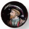 Médaillon en cuivre émaillé, Limoges, XIXᵉ siècle Médaillon circulaire en cuivre émaillé polychrome, représentant un portrait de Henri II, roi de France, de profil à gauche, vêtu d’un riche pourpoint bleu brodé or et coiffé d’un large chapeau à plume. Le fond grenat profond, l’élégance du visage et le raffinement des costumes évoquent les portraits de cour du XVIᵉ siècle. Le rendu minutieux de l’é