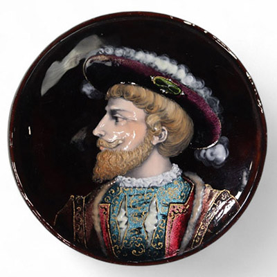 Médaillon en cuivre émaillé, Limoges, XIXᵉ siècle Médaillon circulaire en cuivre émaillé polychrome, représentant un portrait de Henri II, roi de France, de profil à gauche, vêtu d’un riche pourpoint bleu brodé or et coiffé d’un large chapeau à plume. Le fond grenat profond, l’élégance du visage et le raffinement des costumes évoquent les portraits de cour du XVIᵉ siècle. Le rendu minutieux de l’é