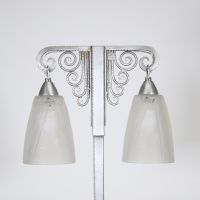 J. Vandôme & Muller Frères Lunéville, vers 1930 Lampe Art Déco à deux lumières en métal martelé nickelé et verrerie signée.  Structure en potence à deux bras terminés par d’élégantes volutes martelées, surmontant un fût vertical en métal à décor rayonnant. La base rectangulaire est signée J. Vandôme, artisan ou maison d’édition réputée pour ses œuvres de ferronnerie décorative dans les années 1930