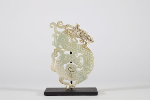 Pendentif en jade vert à décor de deux Chilong, Chine, dans le style des Royaumes combattants Pendentif ajouré en jade vert translucide, finement sculpté d’un décor en léger relief figurant deux dragons chilong entrelacés aux corps sinueux, ponctués de motifs spiralés en bosse. Le traitement du relief, la composition symétrique et la stylisation des têtes évoquent les productions du style archaïsa