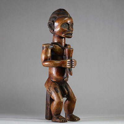 Figure d’ancêtre Fang Mabea ( Byeri), Sud-Cameroun (zones de Kribi, Akom II, Bipindi) . La posture est semi assise, les deux mains jointes tenant une corne de libation, symbole d’offrande aux ancêtres. La coiffure est finement striée, typique du style Fang-Mabea. Un appui dorsal vertical permet de stabiliser la posture. Une scarification frontale est visible entre les sourcils, les prunelles sont