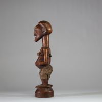 Fétiche rituel figurant un nkishi protecteur ethnie Songye, sous groupe Kalebwe. Figure dotée d'un long cou, de pieds larges, d'un visage souriant et d'une ceinture abdominale contenant une charge organique et présentant autrefois une corne magique au sommet du crâne. Usure rituelle et patine ancienne authentifient son usage. Très belle représentation Kalebwe, entre force symbolique et expressivit