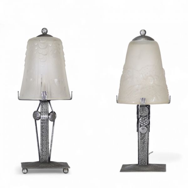 Muller Frères, Lunéville, vers 1930 Ensemble de deux lampes Art Déco en verre moulé-pressé et monture en métal ouvragé à finition nickelée mate.  Chacune des lampes repose sur une base rectangulaire en métal travaillé au repoussé, présentant une surface texturée de motifs géométriques martelés typiques de la période Art Déco. Le fût vertical, orné de pastilles et de stries régulières, soutient une