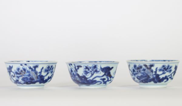 Chine, trois bols en porcelaine bleu et blanc, dynastie Qing, XVIIIe siècle, décorés de fleurs et symboles bouddhiques en léger relief au bleu sous couverte, l’intérieur orné d’une fleurette stylisée.