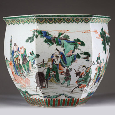 Rare et spectaculaire vase en porcelaine de forme hexagonale, décoré en émaux de la famille verte. Chaque pan du corps présente une scène animée mettant en scène des dignitaires, serviteurs et immortels dans un paysage arboré ponctué de pins, rochers et nuées stylisées. Les personnages, finement détaillés, sont représentés à cheval, à pied ou en conversation, dans un esprit narratif typique de la