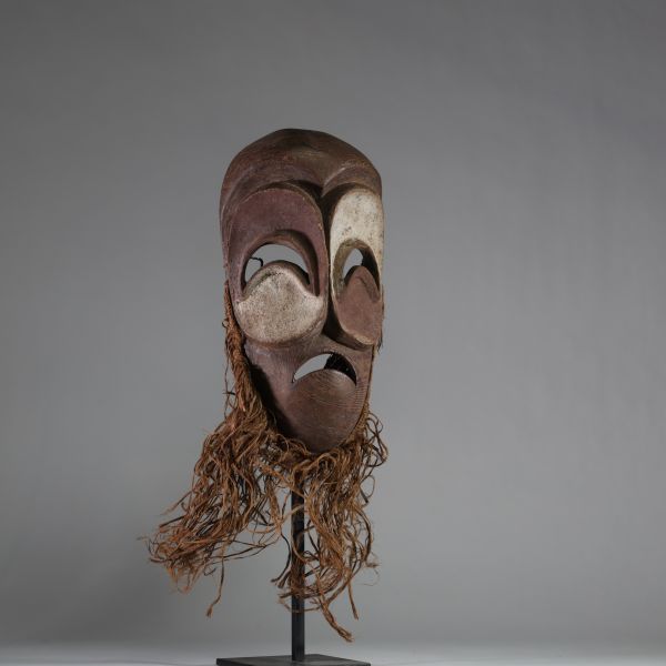 Masque Bembé, RD Congo. Bois, raphia. Présentant des yeux et une bouche en demi-lune, typique de la tradition Bembé (RDC). Polychromie rouge et blanche symbolique, expression dramatique, patine ancienne. Utilisation probable lors de rituels funéraires ou initiatiques. Première moitié du XXe siècle. H : 39 cm.  Collecté sur site par A.S., St Idesbald, début des années 1950