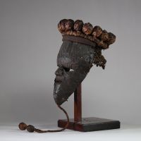 : Masque rituel masculin de haut rang initiatique Salampasu, RD Congo. Le visage est recouvert de feuilles métalliques (cuivre ou laiton). La bouche triangulaire dentée, caractéristique des masques Salampasu, confère à l’objet une forte expressivité rituelle. La coiffe est composée de 28 boules de rotin tressé et la barbe végétale tressée se termine par deux boules identiques. L’intérieur présente