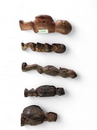 Ensemble de cinq figurines rituelles miniatures Yaka, RD Congo, bois, raphia. H : de 7 à 11 cm. Rare ensemble de petites figurines anthropomorphes utilisées dans le contexte rituel des Yaka (Kwango-Kwilu), au sud-ouest de la RDC. Ces sculptures miniatures, marquées par une forte stylisation et des traces rituelles (pigments, craquelures, dépôt), étaient utilisées comme fétiches de protection ou de