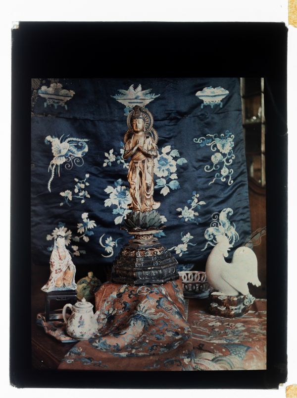 Léon Herlant (1873-1968) — 1 autochrome sur plaque Lumière, 12 x 9 cm.  Dans cette composition minimaliste d’une grande élégance, réalisée vers 1910, se déploie un subtil équilibre entre spiritualité, esthétique et culture de l’objet. Au centre trône un Amida Bouddha debout, sculpté en bois doré, figure emblématique du bouddhisme japonais de la période Edo, porteur de paix intérieure et de sagesse