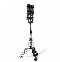 Grande menorah à sept branches en fer forgé, travail juif, vers 1900  Élégante et imposante menorah à sept branches en fer forgé, réalisée par un artisanat juif du début du XXe siècle. La structure finement travaillée, à décor de feuilles stylisées et de volutes, repose sur un piétement tripode à motif végétal. Ce chandelier, emblématique de la tradition rituelle juive