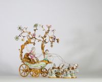 Centre de table à décor de carrosse tiré par quatre chevaux, en bronze ciselé et doré, la scène animée de figures en porcelaine polychrome, représentant deux jeunes enfants dans une calèche ornée de volutes feuillagées et de guirlandes fleuries. Les chevaux sont en porcelaine, fixés sur des bases en porcelaine émaillée à décor fleuri. Travail de style rococo, probablement allemand ou viennois, ver