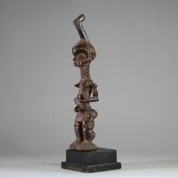 Statuette Bena Lulua, Région du Kasaï RD Congo. Bois. Très belle représentation d’ une figure féminine debout, aux proportions allongées. Tête légèrement surdimensionnée, ornée d'une coiffe cérémonielle monumentale se terminant en crosse verticale. Le visage montre des traits stylisés : yeux en amande, lèvres pleines, nez droit, et scarifications typiques sur le front, les joues et le menton. Le c