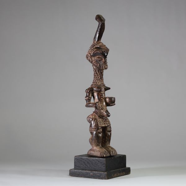 Statuette Bena Lulua, Région du Kasaï RD Congo. Bois. Très belle représentation d’ une figure féminine debout, aux proportions allongées. Tête légèrement surdimensionnée, ornée d'une coiffe cérémonielle monumentale se terminant en crosse verticale. Le visage montre des traits stylisés : yeux en amande, lèvres pleines, nez droit, et scarifications typiques sur le front, les joues et le menton. Le c