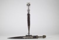 Poignard persan à décor d'argent, début XIXᵉ siècle Poignard oriental monté en argent repoussé et ciselé, présentant une garde et un fourreau richement ornés de motifs floraux et de cartouches géométriques, caractéristiques de l’art décoratif perse. Le pommeau bombé et la garde sont rehaussés de filets floraux, certains émaillés de bleu.  La lame à double tranchant, probablement forgée en acier, e