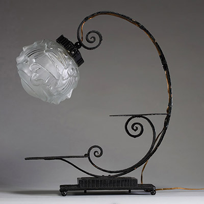 André HUNEBELLE (1896-1985) dans le goût de - Lampe pied fumer en fer forgé martelé et globe en verre moulé pressé à décor de visages de femmes, vers 1920-30.