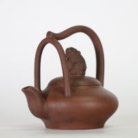 Chine, théière en grès de Yixing à anse surélevée et couvercle orné d’un lion bouddhique, XIXe siècle Théière de forme aplatie en terre cuite brune de Yixing, à anse haute ondulante et bec verseur en 