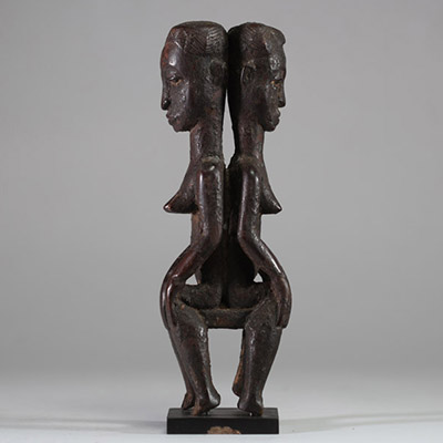 Rare statue Janiforme Akan ( Attié ou Agni) ,Côte d’Ivoire. Bois. Représentation de deux figures féminines assises dos à dos. Les deux têtes présentent une coiffe lobée striée, et les visages sont peints avec des yeux blancs à pupilles noires dilatées. La posture est frontale, hiératique, les mains reposant sur les genoux. La patine est brune à noire, grasse, crouteuse et ancienne, avec traces d'u