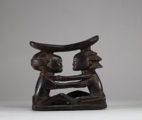 Ancien appui-nuque Luba « Shankadi », Congo RDC. Très bel exemplaire représentant deux figures humaines assises face à face, les bras posés sur les épaules de l’autre, dans une posture d’étreinte rituelle. Chacune soutient une tablette repose-nuque incurvée. L’une des figures présente une coiffure en croix (tulume) et l’autre une coiffure en cascade ( dans la tradition du maître de Kalundwe) . Les