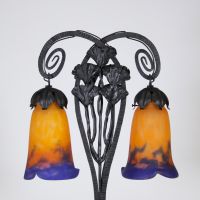 Muller Frères, Lunéville, vers 1905 Lampe à deux lumières en fer forgé martelé à décor de ginkgo biloba et verreries multicouches signées.  Superbe lampe Art Nouveau en fer forgé patiné noir, montée sur une base rectangulaire, s’élevant en double col de cygne à volutes stylisées. Le fût est orné de feuilles et hampes florales de ginkgo biloba, motif emblématique du symbolisme végétal de la Belle É