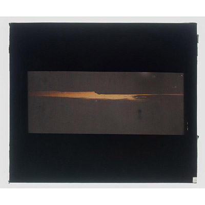 Léon Herlant (1873-1968) — 1 autochrome sur plaque Lumière, 8,5 x 10 cm.  Autochrome d'un coucher ou lever de soleil, circa 1910  Cet autochrome saisit un moment de transformation fugace, où la lumière et l'ombre se battent pour prendre forme. Le coucher ou lever du soleil est ici magnifiquement fragmenté par une falaise imposante et des nuages noirs qui coupent la scène en deux. L’horizon, partie