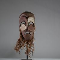 Masque Bembé, RD Congo. Bois, raphia. Présentant des yeux et une bouche en demi-lune, typique de la tradition Bembé (RDC). Polychromie rouge et blanche symbolique, expression dramatique, patine ancienne. Utilisation probable lors de rituels funéraires ou initiatiques. Première moitié du XXe siècle. H : 39 cm.  Collecté sur site par A.S., St Idesbald, début des années 1950