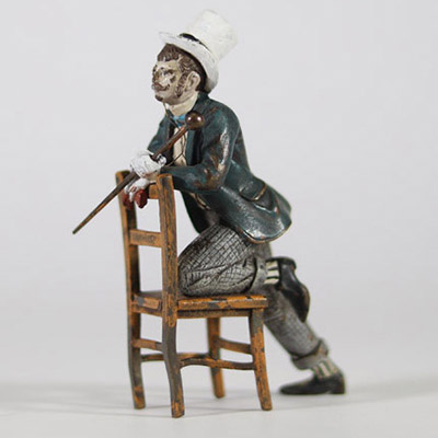 Bronze de Vienne, XIXᵉ siècle Petite figure en bronze polychrome représentant un homme assis à l’envers sur une chaise, vêtu d’un costume bourgeois avec chapeau haut-de-forme, gants blancs et canne. Il s’agit d’un exemple typique des bronzes de Vienne du XIXᵉ siècle, appréciés pour leurs sujets pittoresques, souvent inspirés du théâtre, des scènes de genre ou de la vie citadine.