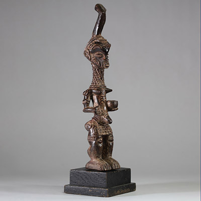 Statuette Bena Lulua, Région du Kasaï RD Congo. Bois. Très belle représentation d’ une figure féminine debout, aux proportions allongées. Tête légèrement surdimensionnée, ornée d'une coiffe cérémonielle monumentale se terminant en crosse verticale. Le visage montre des traits stylisés : yeux en amande, lèvres pleines, nez droit, et scarifications typiques sur le front, les joues et le menton. Le c