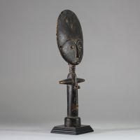 Poupée de fertilité Akua ba, groupe Akan, ethnie Ashanti, Ghana. Tête de forme plate et circulaire, très stylisée, yeux en amande, le nez fin et une petite bouche schématique. Colonne cylindrique avec les bras en croix et base évasée pour la stabilité. Patine riche et matte avec des variations subtiles de couleur, ce qui laisse présager une utilisation sur une longue période. L'arrière du disque d