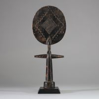 Poupée de fertilité Akua ba, groupe Akan, ethnie Ashanti, Ghana. Tête de forme plate et circulaire, très stylisée, yeux en amande, le nez fin et une petite bouche schématique. Colonne cylindrique avec les bras en croix et base évasée pour la stabilité. Patine riche et matte avec des variations subtiles de couleur, ce qui laisse présager une utilisation sur une longue période. L'arrière du disque d