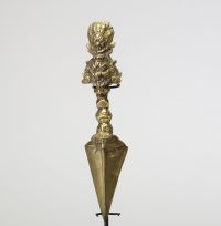 Poignard rituel bouddhique, dit phurba, en bronze doré, à triple lame triangulaire. Le manche est orné d’un nœud symbolique à facettes et se termine par une représentation expressive de Vajrakilaya. Travail tibétain, XIXe siècle.