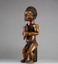 Figure d’ancêtre Fang Mabea ( Byeri), Sud-Cameroun (zones de Kribi, Akom II, Bipindi) . La posture est semi assise, les deux mains jointes tenant une corne de libation, symbole d’offrande aux ancêtres. La coiffure est finement striée, typique du style Fang-Mabea. Un appui dorsal vertical permet de stabiliser la posture. Une scarification frontale est visible entre les sourcils, les prunelles sont