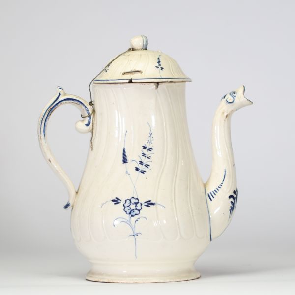 Boch Luxembourg, vers 1790–1810 Cafetière en faïence fine ivoire à décor bleu sous couverte Cafetière à panse godronnée et décor peint en bleu de bouquets stylisés, feuillages et frises. Bec zoomorphe à décor stylisé, anse sinueuse soulignée de filets. Couvercle à prise en toupie, chaînette d’origine reliant couvercle et anse. Élégant modèle typique des premières productions de la manufacture de S