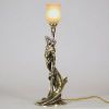 Raoul François Louche (actif au début du XXe siècle) Lampe Art Nouveau en bronze doré et patiné, verrerie signée Schneider  Rare et délicate lampe de table en bronze à patine nuancée représentant une femme nue, élancée et drapée dans un mouvement tourbillonnant, typique du style naturaliste et sensuel de l’Art Nouveau. Le personnage féminin s’élève avec grâce pour former le corps du luminaire, ses