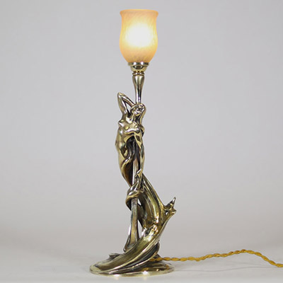 Raoul François Louche (actif au début du XXe siècle) Lampe Art Nouveau en bronze doré et patiné, verrerie signée Schneider  Rare et délicate lampe de table en bronze à patine nuancée représentant une femme nue, élancée et drapée dans un mouvement tourbillonnant, typique du style naturaliste et sensuel de l’Art Nouveau. Le personnage féminin s’élève avec grâce pour former le corps du luminaire, ses