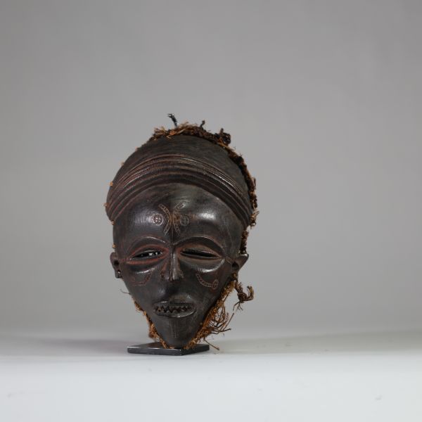 Ancien masque tribal avec coiffe « Mwana pwo » Chokwe/ Tshokwe, RD Congo, Angola. Bois. Très bel exemplaire bien conforme avec les yeux mi clos en « amande », le nez fin et allongé, la bouche entre-ouverte avec des dents « limées ». La coiffe ( samunganda) en raphia est élaborée et symbolise la coiffure des femmes de haut rang.  La patine est profondeet typique des masques ayant été frottés avec d