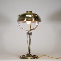 France, vers 1900 Lampe de table Art Nouveau en laiton, capeline ajourée et piétement à cabochons de verre coloré.  Cette lampe décorative de la période Art Nouveau présente une élégante silhouette élancée en laiton doré, avec un fût nervuré à lignes fluides convergeant vers une base circulaire décorée de cabochons de verre sertis en vert, rouge, ambre et jaune, typiques de l’ornementation polychr
