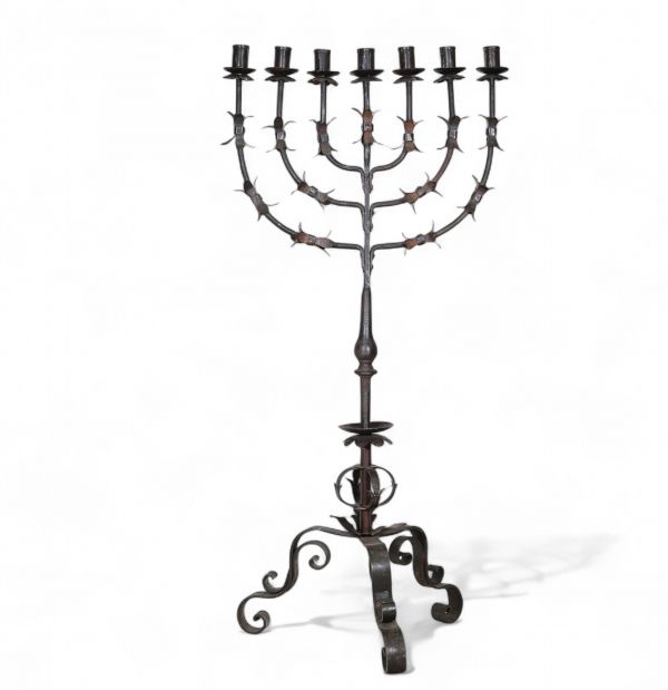 Grande menorah à sept branches en fer forgé, travail juif, vers 1900  Élégante et imposante menorah à sept branches en fer forgé, réalisée par un artisanat juif du début du XXe siècle. La structure finement travaillée, à décor de feuilles stylisées et de volutes, repose sur un piétement tripode à motif végétal. Ce chandelier, emblématique de la tradition rituelle juive