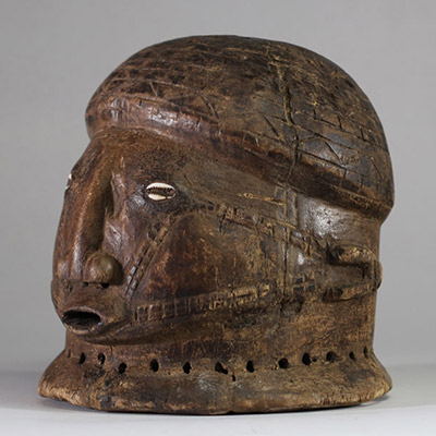 Masque-casque en bois, de forme hémisphérique Tabwa, RD congo. Visage sculpté avec un nez droit, saillant, de forme anguleuse, très caractéristique des styles Tabwa et Luba-Tabwa. Les yeux sont incrustés de cauris, Les scarifications faciales linéaires et parallèles, courant des tempes vers la bouche, sont typiques des traditions Tabwa. La patine naturelle, les abrasions autour de la base perforée