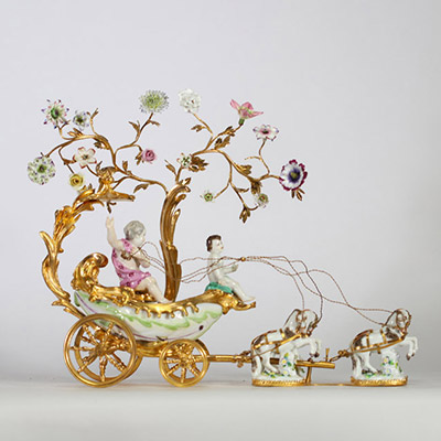 Centre de table à décor de carrosse tiré par quatre chevaux, en bronze ciselé et doré, la scène animée de figures en porcelaine polychrome, représentant deux jeunes enfants dans une calèche ornée de volutes feuillagées et de guirlandes fleuries. Les chevaux sont en porcelaine, fixés sur des bases en porcelaine émaillée à décor fleuri. Travail de style rococo, probablement allemand ou viennois, ver