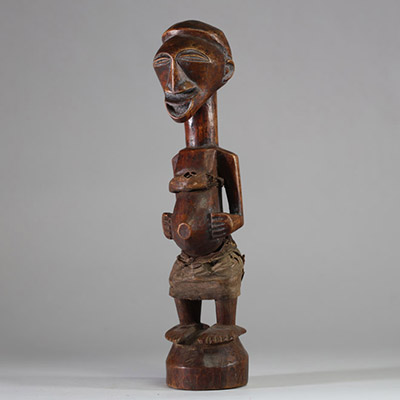 Fétiche rituel figurant un nkishi protecteur ethnie Songye, sous groupe Kalebwe. Figure dotée d'un long cou, de pieds larges, d'un visage souriant et d'une ceinture abdominale contenant une charge organique et présentant autrefois une corne magique au sommet du crâne. Usure rituelle et patine ancienne authentifient son usage. Très belle représentation Kalebwe, entre force symbolique et expressivit