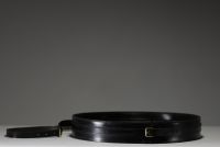 Jacques ADNET (1900-1984) Wall-mounted mirror with circular metal frame entirely sheathed in black leather, fastening strap ending in a brass buckle, circa 1950.