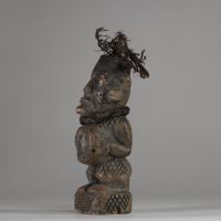 Ancienne figure rituelle en pierre  Bakongo, RD Congo. Travail de sculpture très fin. Le personnage a les mains posées sur le bilogo, protégé par un morceau de miroir. Le sommet du crâne est creusé et contient des plumes anciennes, renforçant sa dimension rituelle. Les jambes, le dos et les joues présentent des motifs gravés en croisillons, typiques de l'art Yombe. Un cordon textile est encore vis
