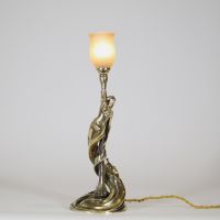 Raoul François Louche (actif au début du XXe siècle) Lampe Art Nouveau en bronze doré et patiné, verrerie signée Schneider  Rare et délicate lampe de table en bronze à patine nuancée représentant une femme nue, élancée et drapée dans un mouvement tourbillonnant, typique du style naturaliste et sensuel de l’Art Nouveau. Le personnage féminin s’élève avec grâce pour former le corps du luminaire, ses
