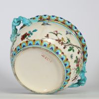 Théodore Deck (1823–1891) Importante jardinière en faïence émaillée, à décor polychrome d’inspiration extrême-orientale représentant un coq, des oiseaux, des papillons et des branchages fleuris en léger relief, sur fond crème. Frise supérieure ornée de motifs géométriques bleus et or. Ansés latérales en forme de dragons stylisés émaillés turquoise.