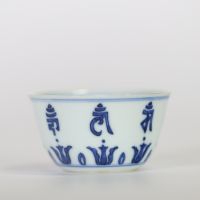 Chine, petit bol en porcelaine bleu et blanc à décor extérieur de caractères bouddhiques stylisés alternant avec des lotus, l’intérieur orné d’une fleur centrale, marque apocryphe à six caractères de 