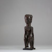 Rare statue Janiforme Akan ( Attié ou Agni) ,Côte d’Ivoire. Bois. Représentation de deux figures féminines assises dos à dos. Les deux têtes présentent une coiffe lobée striée, et les visages sont peints avec des yeux blancs à pupilles noires dilatées. La posture est frontale, hiératique, les mains reposant sur les genoux. La patine est brune à noire, grasse, crouteuse et ancienne, avec traces d'u